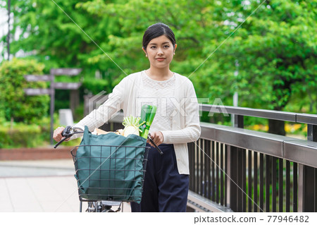 A young woman walking while pulling a shopping bag in a bicycle basket 77946482