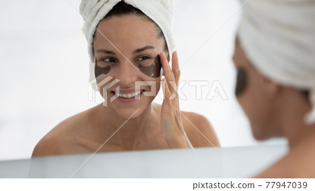 Happy woman applying gel patches for treatment under eye bags 77947039