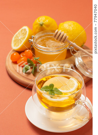 Ginger tea with mint and lemon. Healthy and hot drink. Liquid honey in honey-jar. Crystal cup on bright background. Selective focus. Ginger tea with mint and lemon. Healthy and hot drink. Liquid honey in honey-jar. Crystal cup on bright background. Selective focus. 77947040