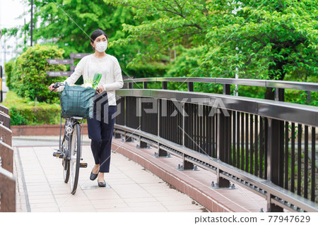 A young woman walking while pulling a shopping bag in a bicycle basket 77947629