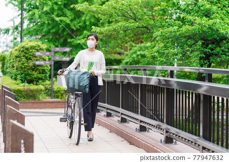 A young woman walking while pulling a shopping bag in a bicycle basket 77947632