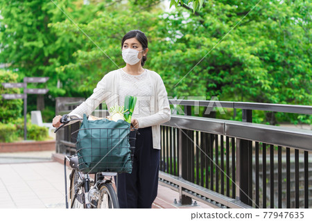 一位年輕女子提著自行車籃裡的購物袋行走 一位年輕女子提著自行車籃裡的購物袋行走 77947635