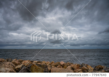 A beautiful, dramatic sky over the ocean. Stones in a wave breaker in the foreground A beautiful, dramatic sky over the ocean. Stones in a wave breaker in the foreground 77947640