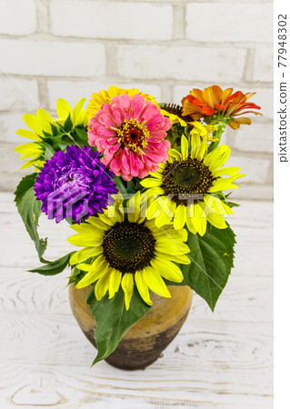 Bouquet of flowers in antique rustic clay jug against white brick wall Bouquet of flowers in antique rustic clay jug against white brick wall 77948302
