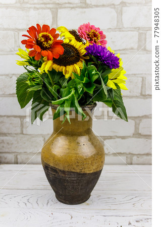 Bouquet of flowers in antique rustic clay jug against white brick wall Bouquet of flowers in antique rustic clay jug against white brick wall 77948305