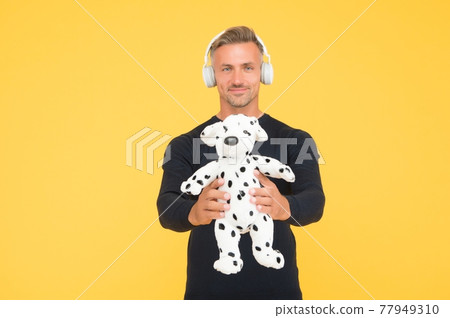 Happy childish middle-aged man listen to music in headphones holding dalmatian toy  77949310