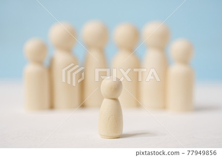 Wooden faceless figures of man in the center and people behind him. 77949856