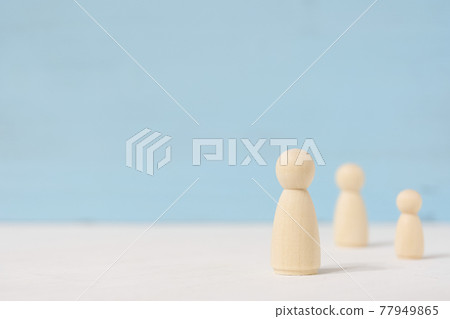 Three faceless wooden toy figures stand apart from each other with copy space. 77949865