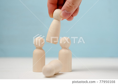 Hand puts or removes wooden figure in the center of two figures. Hand puts or removes wooden figure in the center of two figures. 77950108