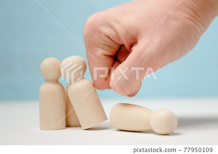 Hand destroying group of wooden figures of people. 77950109