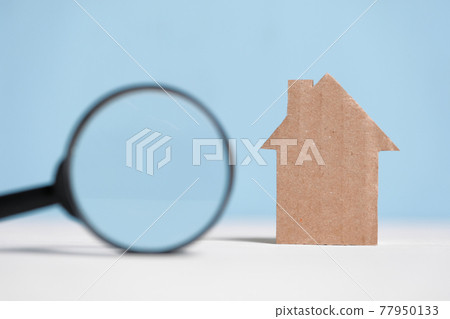 Abstract cardboard house next to a magnifier. Real Estate Search Concept. 77950133