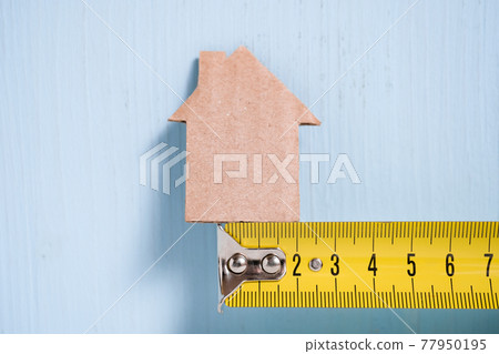 Cardboard cutout house on metal measuring tape on blue background. 77950195