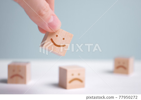 A man holds a wooden cube with a picture of a positive face on the background of negative emotions. 77950272