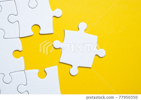 Final white piece is lying next to the jigsaw puzzle on yellow background. Final white piece is lying next to the jigsaw puzzle on yellow background. 77950350