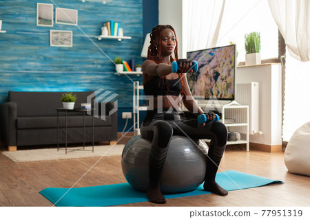 African woman using stability ball keeping outstretched arms African woman using stability ball keeping outstretched arms 77951319
