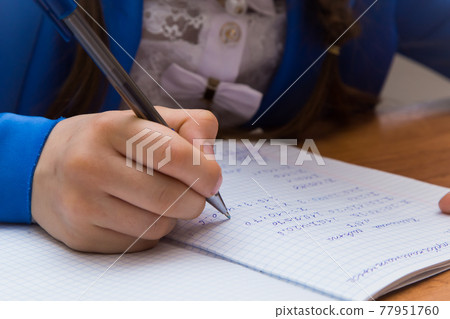 Close-up of a girl's hand with a ballpoint pen writes in a notebooke.  77951760