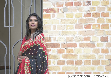 Portrait of a beautiful and smiling Indian woman wearing red saree. 77952472