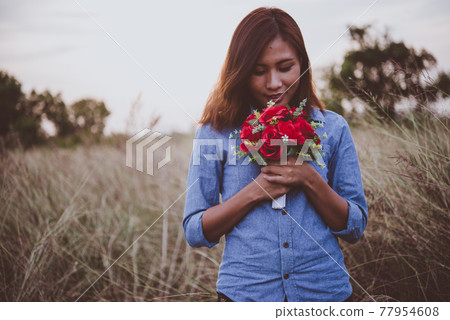 Young hipster woman in field holding a bouquet of red rose, summer holiday. Freedom enjoy lifestyle. Vintage tone. Young hipster woman in field holding a bouquet of red rose, summer holiday. Freedom enjoy lifestyle. Vintage tone. 77954608