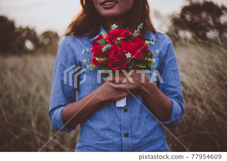 Young hipster woman in field holding a bouquet of red rose, summer holiday. Freedom enjoy lifestyle. Vintage tone. Young hipster woman in field holding a bouquet of red rose, summer holiday. Freedom enjoy lifestyle. Vintage tone. 77954609