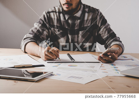 Young businessman writes in a notebook while working analysis business data in office. Young businessman writes in a notebook while working analysis business data in office. 77955668