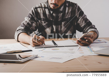 Young businessman writes in a notebook while working analysis business data in office. 77955669
