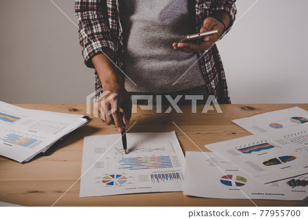 Business Woman with working analysis business document chart and graph while using phone with client. 77955700