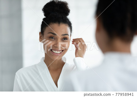 Happy girl in bathrobe cleaning ears with cotton swab 77958941