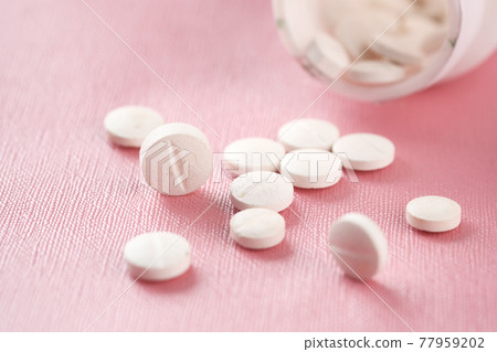 Close up of many while color medical pills spilling on pink  77959202