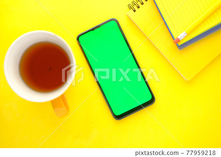 top view of smart phone, coffee mug and notepad on yellow background  77959218