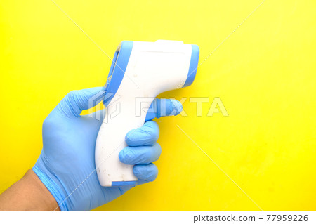 Hand holding infrared thermometer against yellow background  77959226