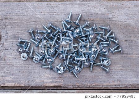 Pile of metal screws on rustic wooden background. 77959495