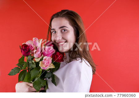 The concept of Valentine's Day and Women's Day. Happy young girl holding a bouquet of roses. The concept of Valentine's Day and Women's Day. Happy young girl holding a bouquet of roses. 77960360