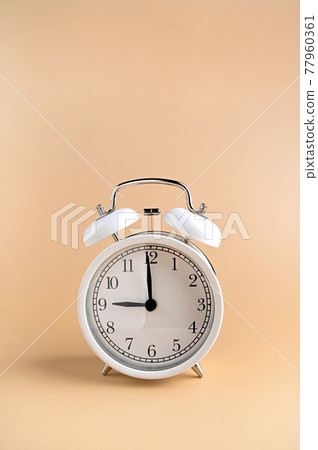 White alarm clock with arrows at nine in the morning. Vintage watch on a beige background. 77960361
