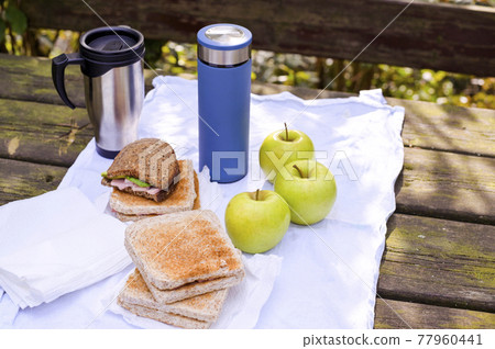 Lunch in the park on an old wooden table. Sandwiches, apples and coffee in a thermos. Lunch in the park on an old wooden table. Sandwiches, apples and coffee in a thermos. 77960441