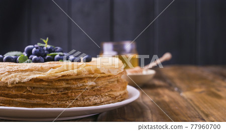 Pancakes with blueberries and honey on a plate, on wooden roofing. Traditional pastries for the 77960700