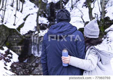 Young woman and man cuddling in a snowy forest. A pair of lovers in winter clothes. The girl holds a Young woman and man cuddling in a snowy forest. A pair of lovers in winter clothes. The girl holds a 77960760