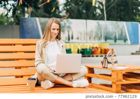 Business woman in blazer working at laptop outside. 77962129
