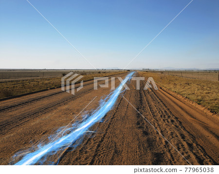 Blue streak of light on dirt road against clear sky 77965038