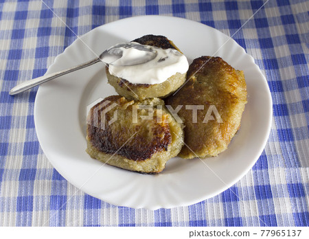 A plate with a Belarusian dish potato pancakes with meat filling and sour cream. Blue checkered background, kalduny 77965137