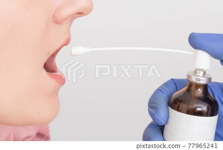 The doctor sprays a local anesthetic to the female patient for a medical procedure. Concept of throat freezing during fibrogastroscopy, close-up 77965241