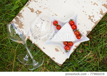 two glasses, cheese and tomatoes on a plate on grass 77966839
