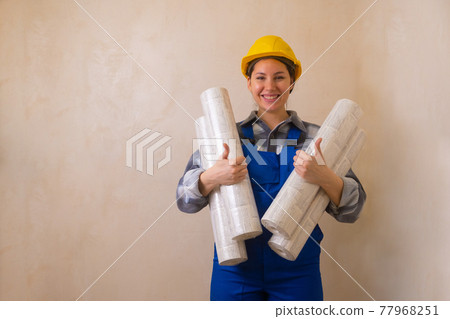 Beautiful brunette construction worker girl holds wallpaper in her hands, smiles and shows thumbs up Beautiful brunette construction worker girl holds wallpaper in her hands, smiles and shows thumbs up 77968251