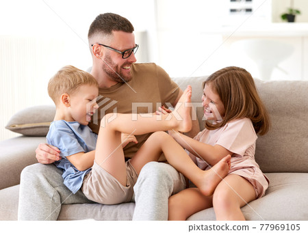 Positive happy family of three enjoying carefree time together at home, dad playing with kids Positive happy family of three enjoying carefree time together at home, dad playing with kids 77969105