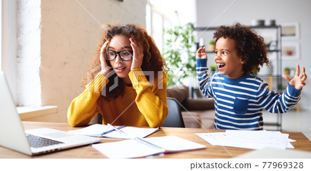 Frustreted african mom trying to work with little kid at home 77969328