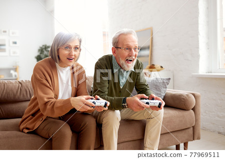 Excited senior couple playing video console games at home Excited senior couple playing video console games at home 77969511