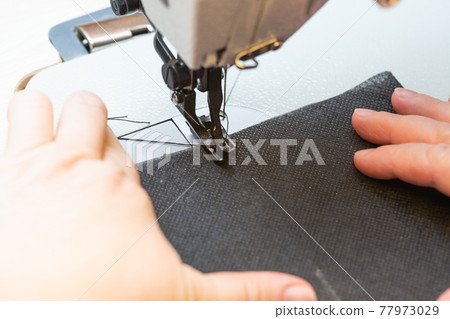 A woman seamstress sews a black cloth on an industrial sewing machine A woman seamstress sews a black cloth on an industrial sewing machine 77973029