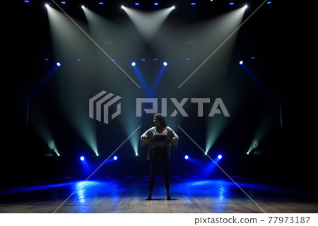 Girl in black suit performing on stage with bright blue background Girl in black suit performing on stage with bright blue background 77973187