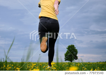 A girl in a yellow T-shirt moves across the field with flowers. Yellow flowers, green grass, blue sky, oak. Travel outside the city. Leisure A girl in a yellow T-shirt moves across the field with flowers. Yellow flowers, green grass, blue sky, oak. Travel outside the city. Leisure 77973540