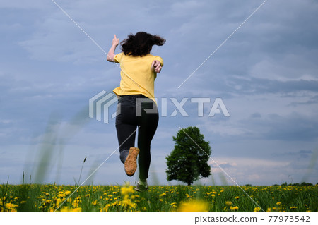 A girl in a yellow T-shirt moves across the field with flowers. Yellow flowers, green grass, blue sky, oak. Travel outside the city. Leisure A girl in a yellow T-shirt moves across the field with flowers. Yellow flowers, green grass, blue sky, oak. Travel outside the city. Leisure 77973542