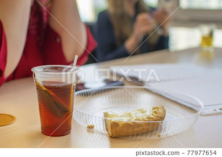 a cup of tea and a piece of cake are lying on the office table near the two dining girls 77977654